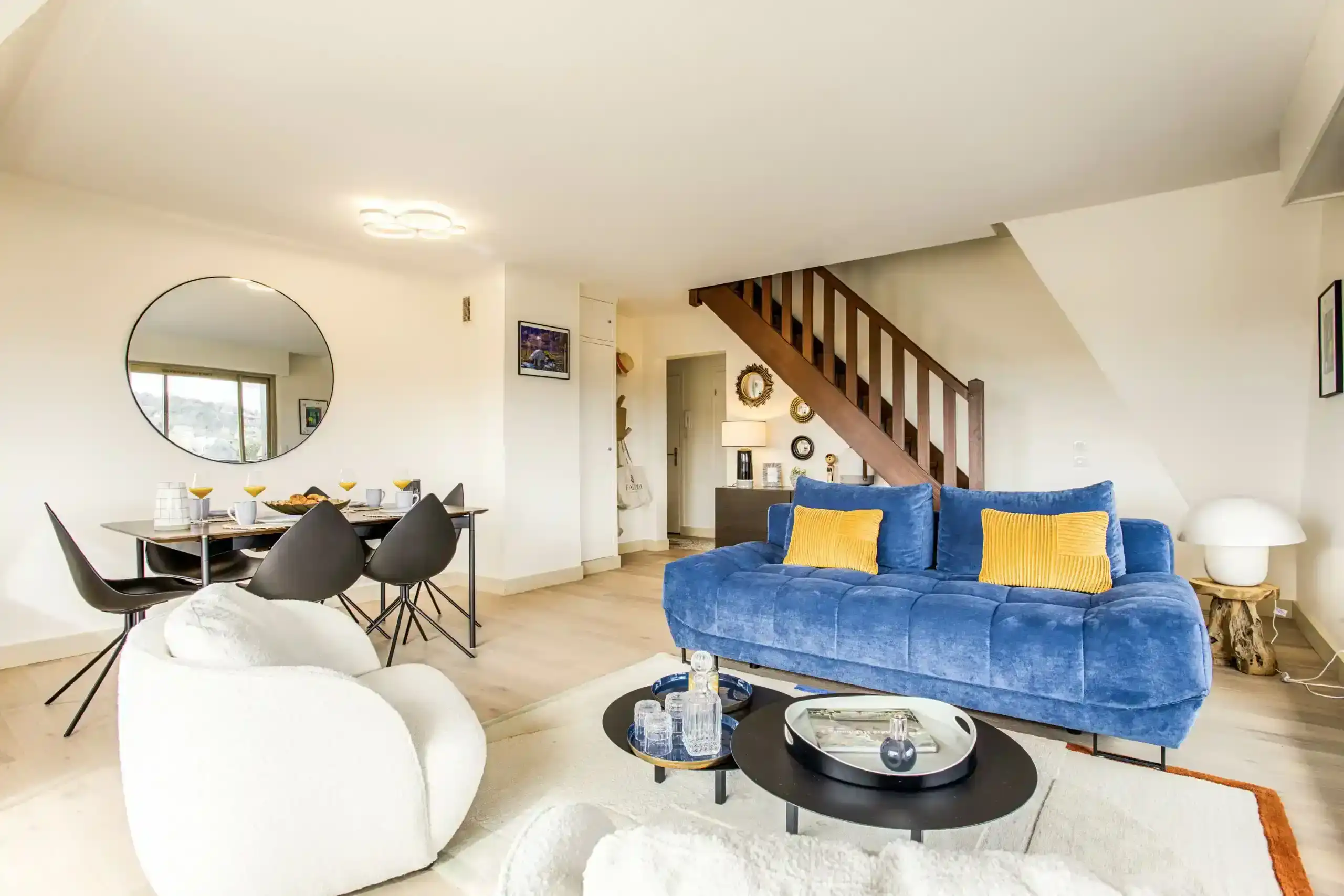 Appartement-ciel-mer-salon-escalier-duplex Salon lumineux avec canapé bleu, salle à manger et escalier en bois dans l’appartement Ciel et Mer