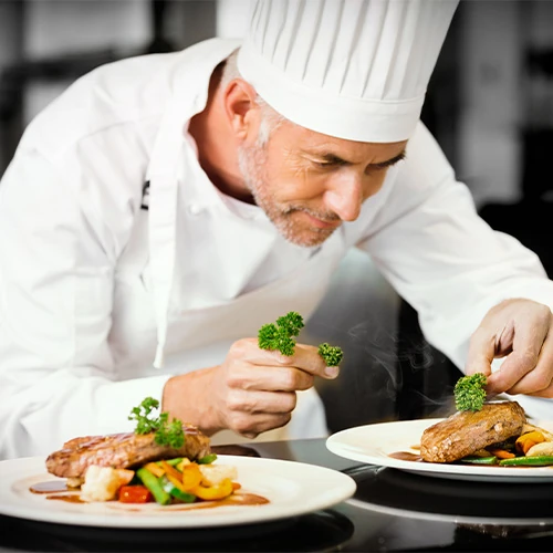 Chef cuisinier à domicile – Repas gastronomique sur mesure Chef professionnel en train de dresser des assiettes gastronomiques, symbole du service de restauration privée offert par la conciergerie