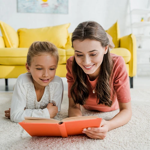 Service de baby-sitting personnalisé à domicile – Conciergerie Deauville Jeune femme lisant un livre avec une enfant dans un salon lumineux, illustrant un service de garde d’enfants à domicile proposé par la conciergerie privée