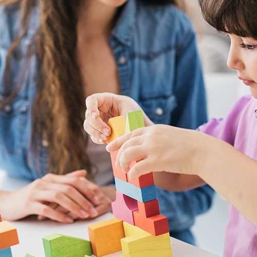 Service de baby-sitting sur mesure à Deauville Enfant jouant avec des blocs colorés sous la surveillance d’une baby-sitter – prestation de garde d’enfants proposée par la conciergerie privée à Deauville